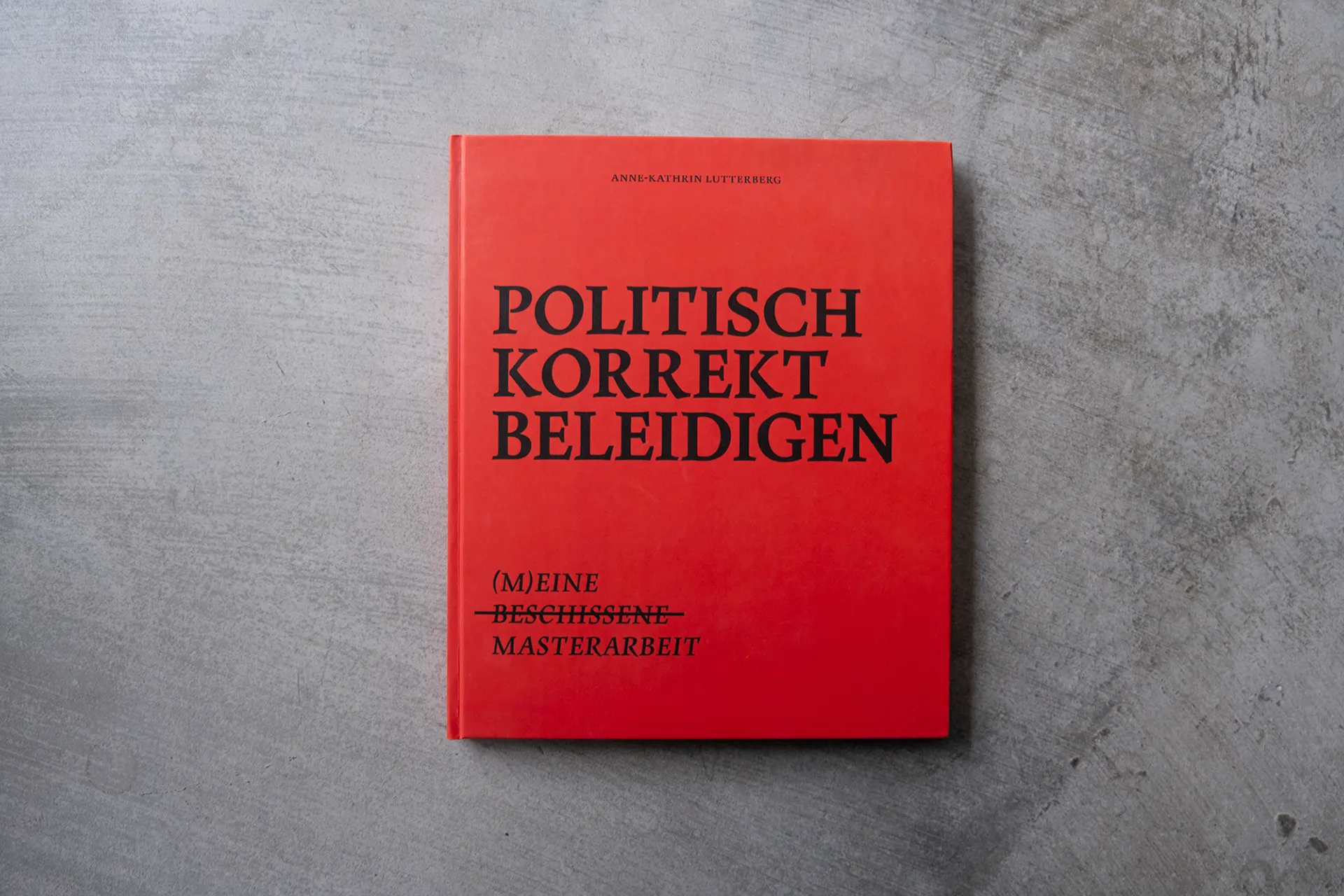 Rotes Buchcover mit dem Titel „Politisch korrekt beleidigen“ auf grauem Beton