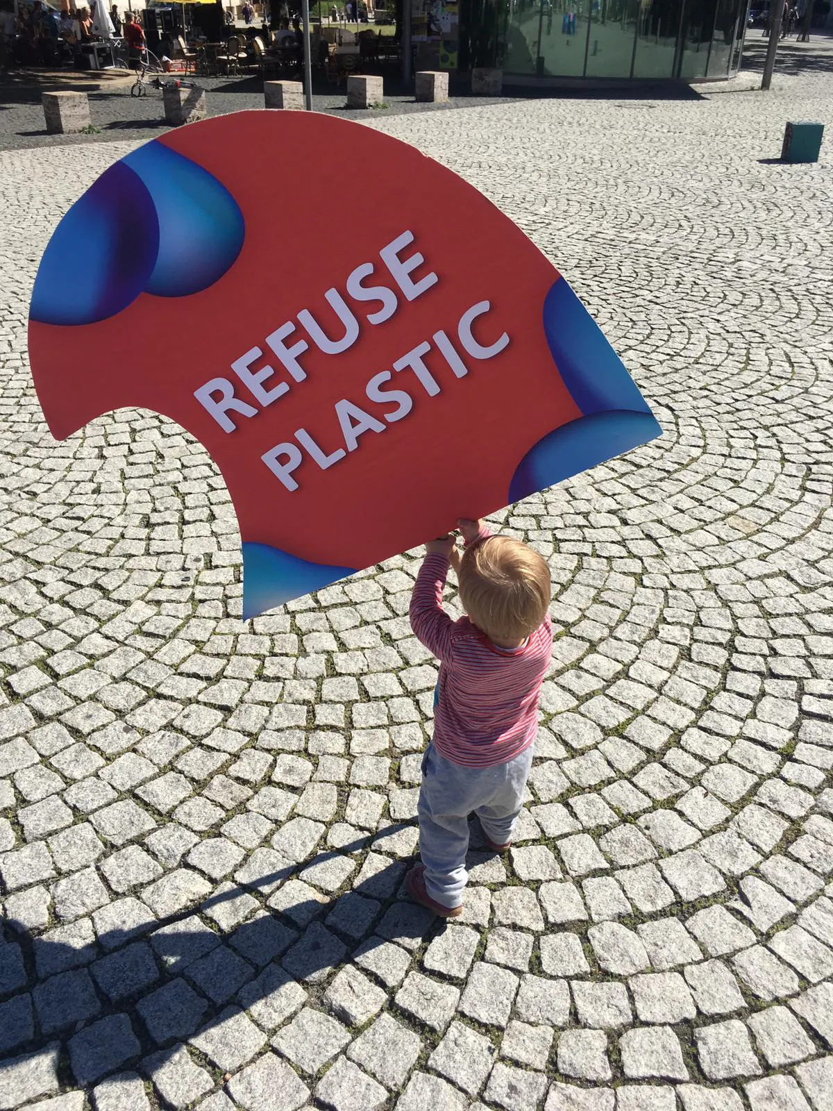 Ein Kind trägt ein wellenförmiges Schild mit der Aufschrift „Refuse Plastic“
