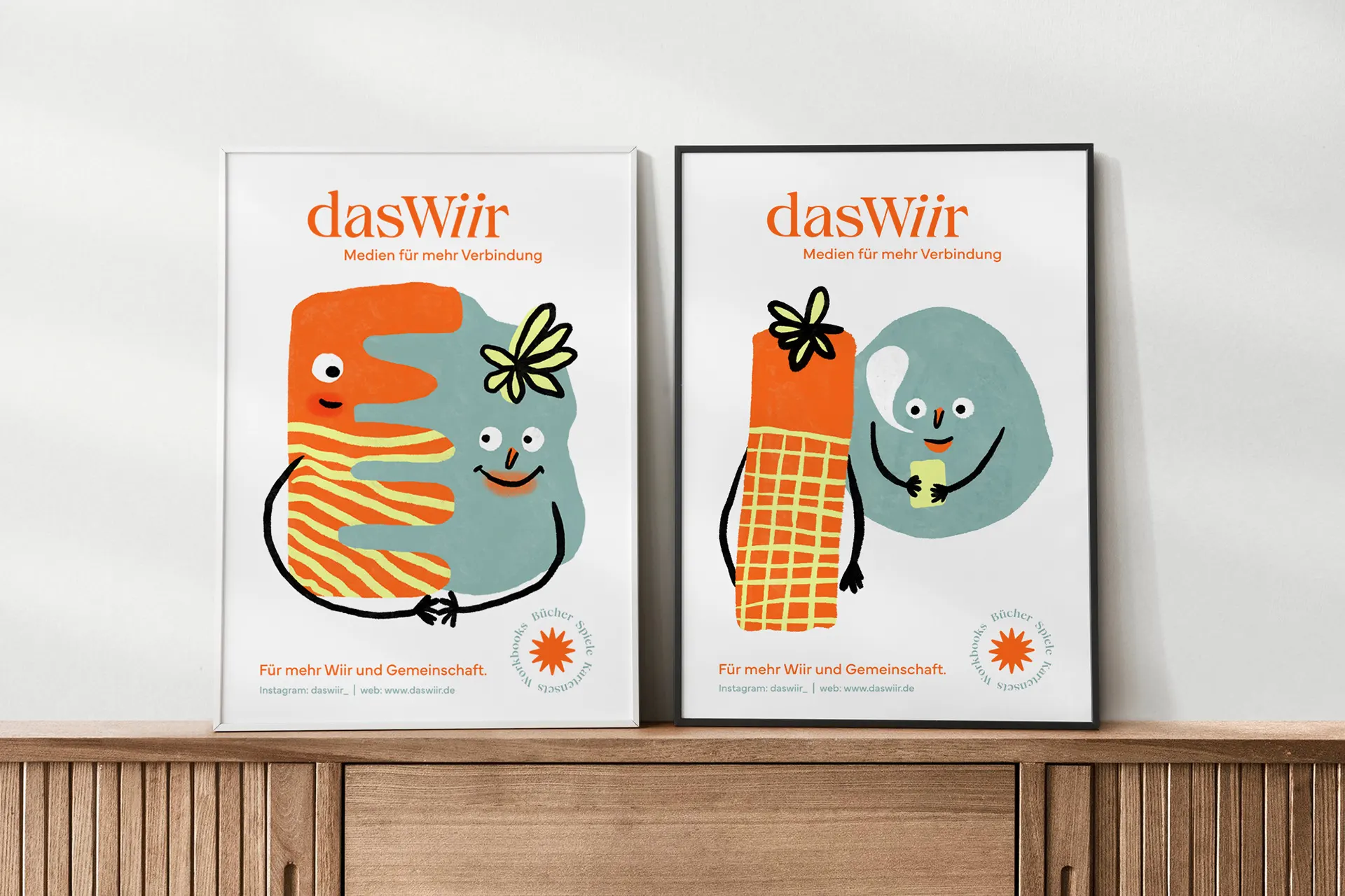 Zwei gerahmte dasWiir-Plakate mit illustrierten Figuren auf einem Holzsideboard