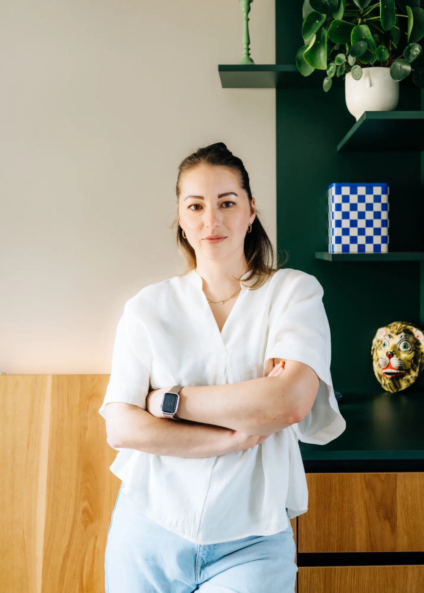 Anne Lutterberg mit verschränkten Armen vor einem dunkelgrünen Regal mit Pflanzen