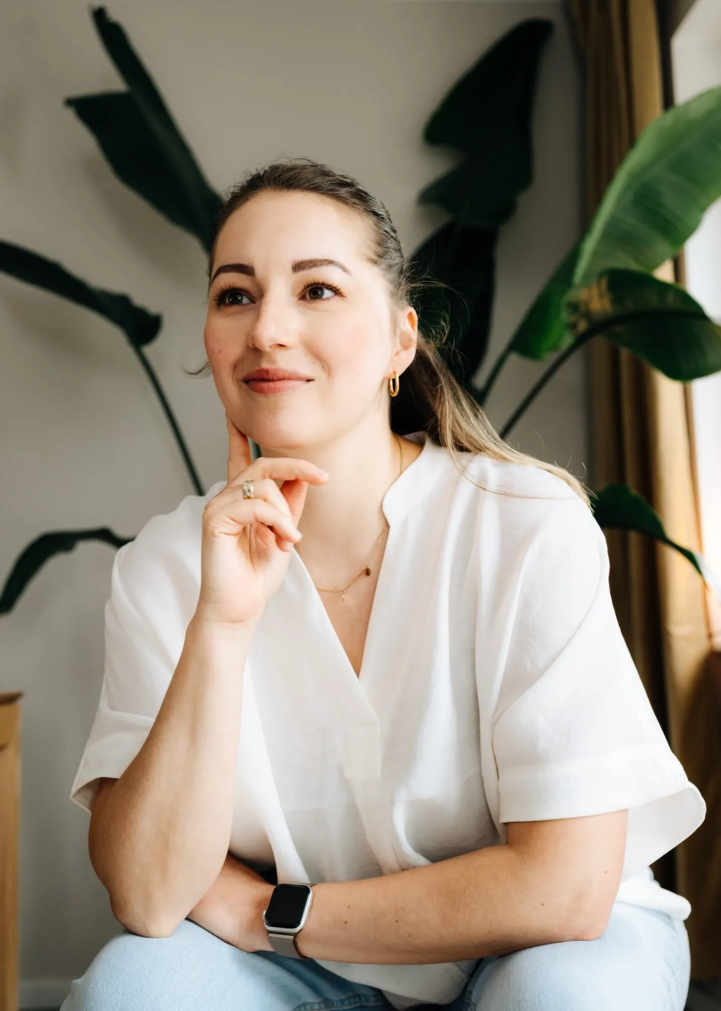 Anne Lutterberg in weißer Bluse, das Kinn auf die Hand gestützt, vor großen Pflanzenblättern